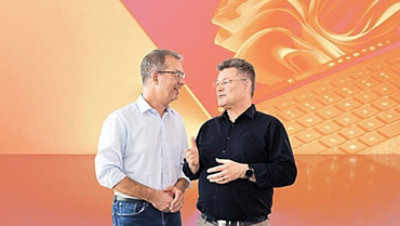 Zwei Männer unterhalten sich vor abstraktem, orangefarbenem Hintergrund, der einen Laptop darstellt.