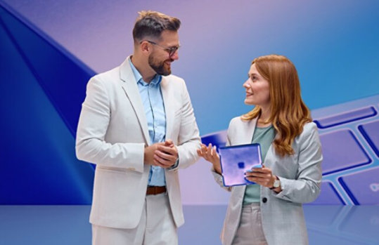 Ein Mann und eine Frau unterhalten sich, die Frau hält ein Tablet. Im Hintergrund ist eine Tastatur zu sehen.