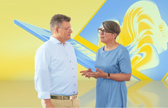 Ein Mann und eine Frau unterhalten sich in einem Studio vor einem gelb-blauen, abstrakten Hintergrund.