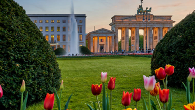 The Brandenburg Gate in Berlin. In front of the gate is a lawn where tulips are blooming.