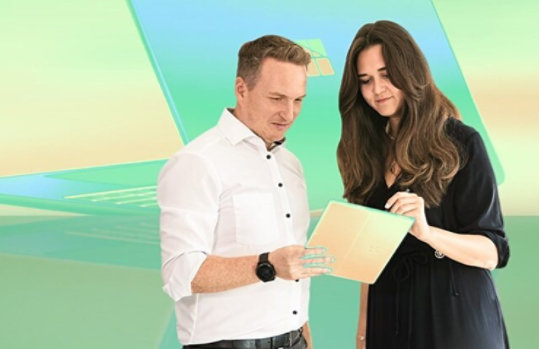 Zwei Geschäftsleute betrachten ein Dokument vor einem blauen und grünen Hintergrund mit Windows-Logo.