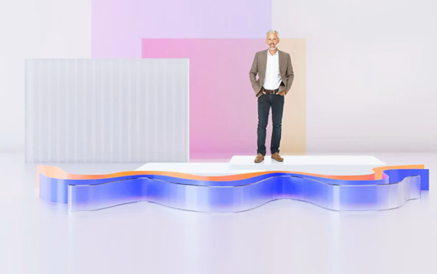 Person auf einer minimalistischen Bühne vor pastellfarbenen geometrischen Elementen und einer beleuchteten blauen, wellenförmigen Struktur im Vordergrund.