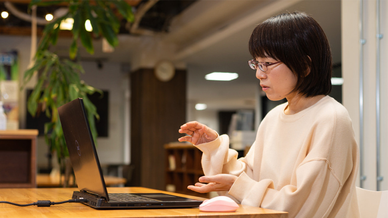 小幡さんの金沢さんは、手のジェスチャーを使って仮想会議で何かを説明するラップトップの前に座っています