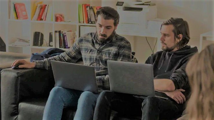 ソファに座りノート PC を見る 2 人の男性