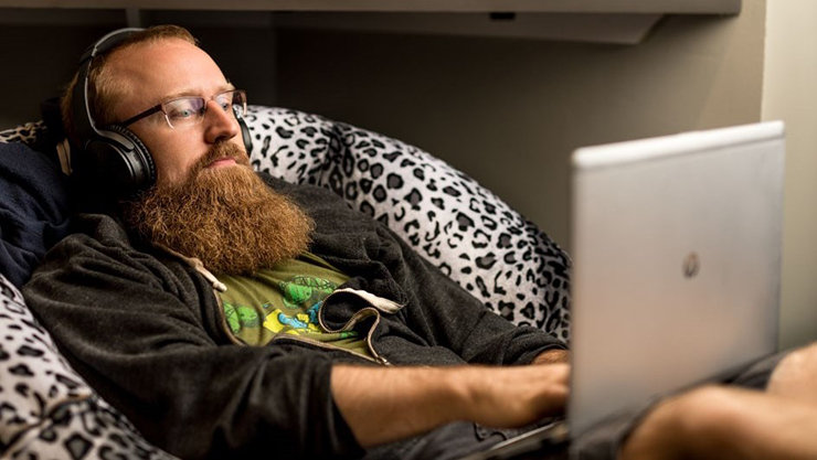 男性がソファでくつろぎ、ヘッドフォンを着用し、ラップトップを操作している