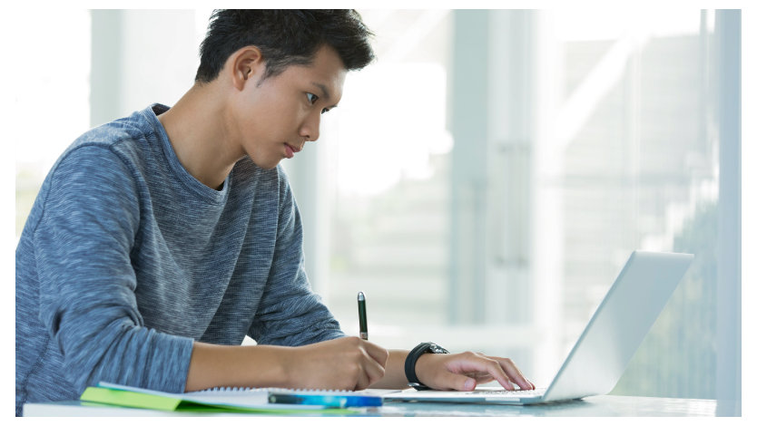 ノート PC を操作しながらノートにメモを取る学生