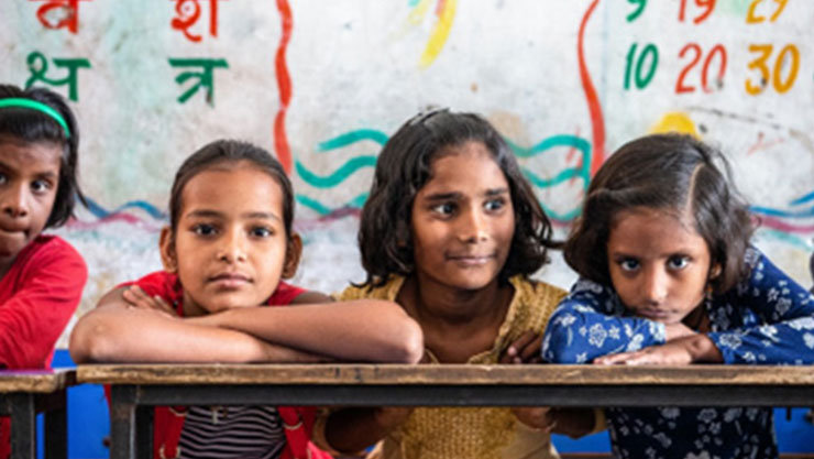 4 girl students in a classroom with3 looking into the camera and 1 looking away