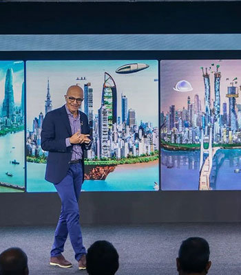 Satya Nadella walking on a stage with his presentation in the background