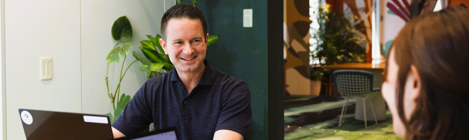 後ろに観葉植物が見える社内で他の人と笑顔で話しているJason