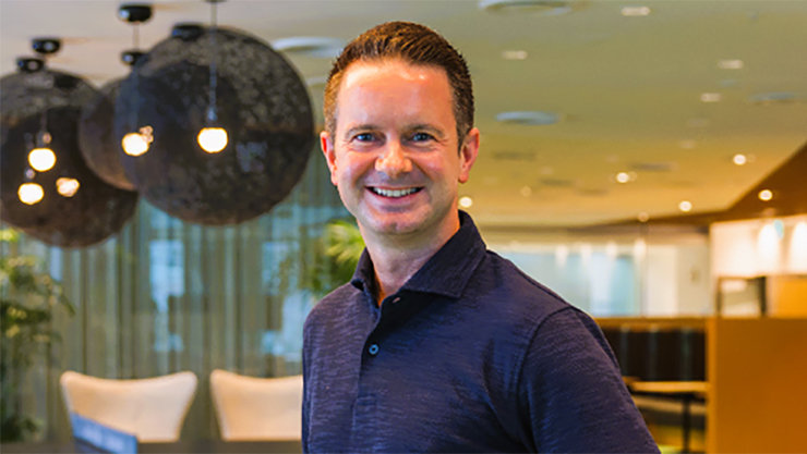 黒くて丸い照明器具が後ろに見えている室内で笑顔で立っているJason