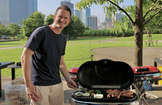 ビルが後ろに見える屋外でバーベキューを楽しむJason