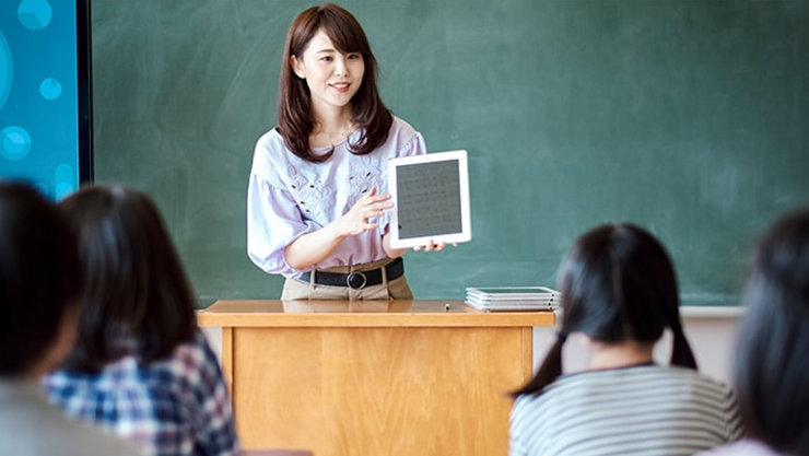 教壇に立ってタブレットで説明する小学校の先生