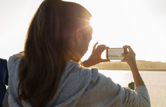 スマホでビーチで日の出の写真を撮る女性