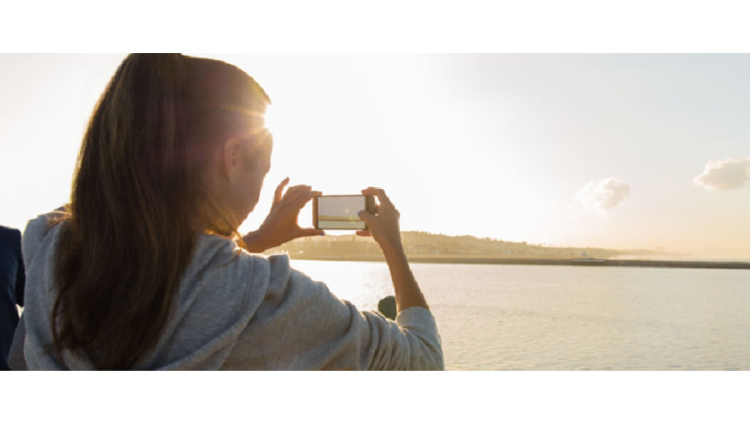 スマホでビーチで日の出の写真を撮る女性