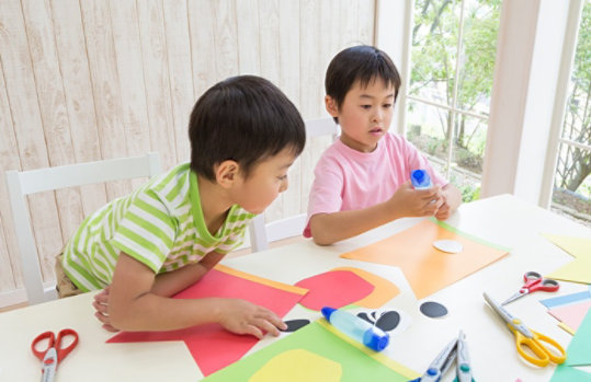 2人の男の子がテーブルの上でアートクラフトを作るために遊んでいます