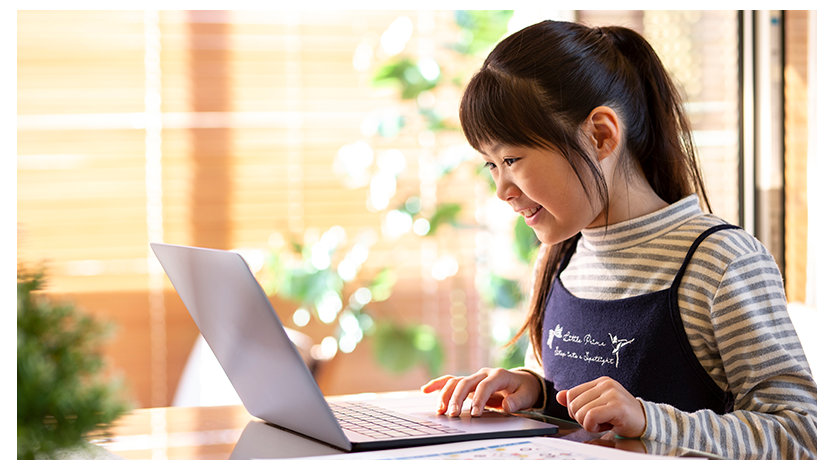 笑顔でノート PC を操作する小学生