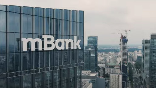budynek z logo mBanku na pierwszym planie po lewej i widok na budynki w centrum Warszawy na dalszym planie po prawej stronie zdjęcia