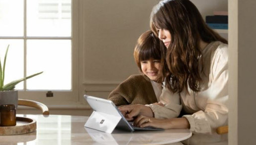 Matka i kilkuletnie dziecko siedzą uśmiechnięci przy stole przed komputerem