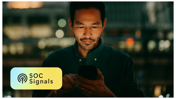 夜の街の明かりを背景に、一人の男性がスマートフォンを見つめている。画面左下には、「SOC Signals」という文字が表示されている。