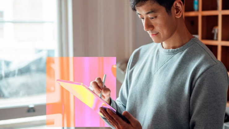  灰色のスウェットシャツを着た男性がスタイラスを使ってタブレットを操作しています。