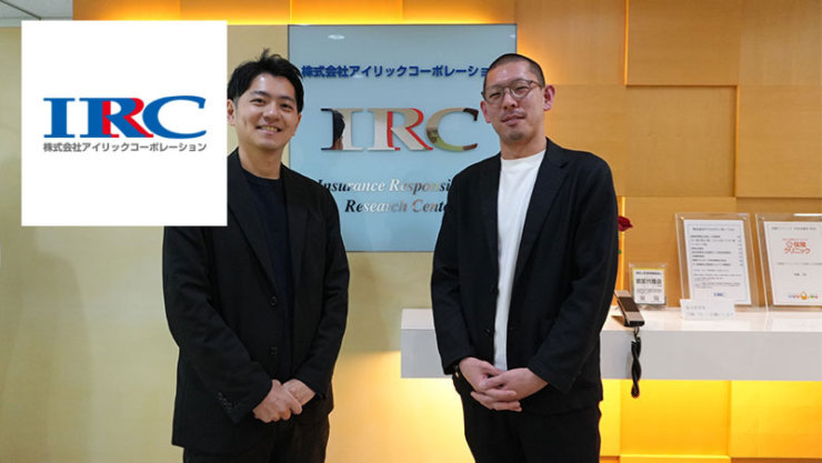 株式会社アイリックコーポレーション の受付エリアで、IRCロゴの前に立つ2名のビジネスパーソン
