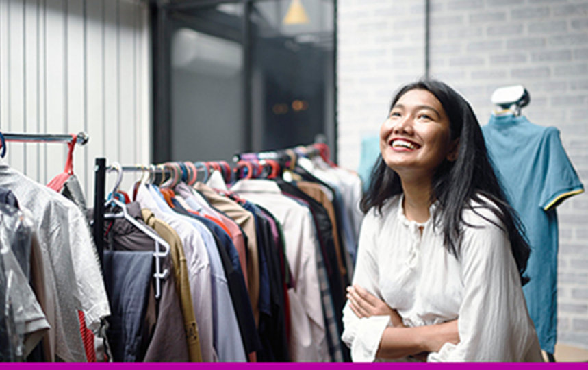 Female business owner smiling next to a rack of clothes.