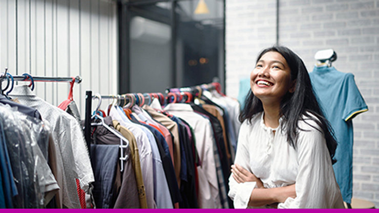 Female business owner smiling next to a rack of clothes.