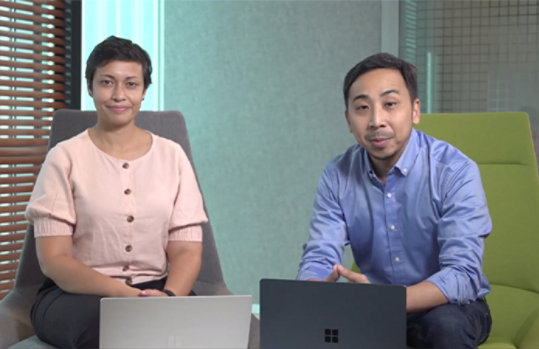 Two colleagues are sitting on chairs with their laptops in front of them
