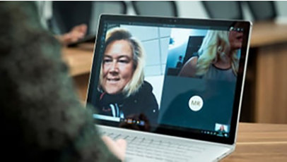 Person in at a desk in a conference room using a Surface laptop to make a Microsoft Teams video call with three other people. Business Voice, conference call, online meeting, remote meeting