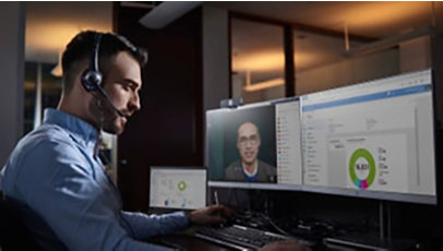 Male IT professional at desk with multiple devices, chatting on teams with a headset.