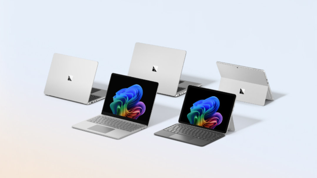 5台のシルバーのMicrosoft Surfaceデバイス。手前の2台は画面が開いており、カラフルなWindows 11の壁紙が表示されています。