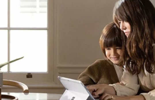 女性と子供がキッチンカウンターでタブレットを使いながら笑顔を見せており、近くにはオレンジの入ったボウルとアロエの鉢植えがあります。