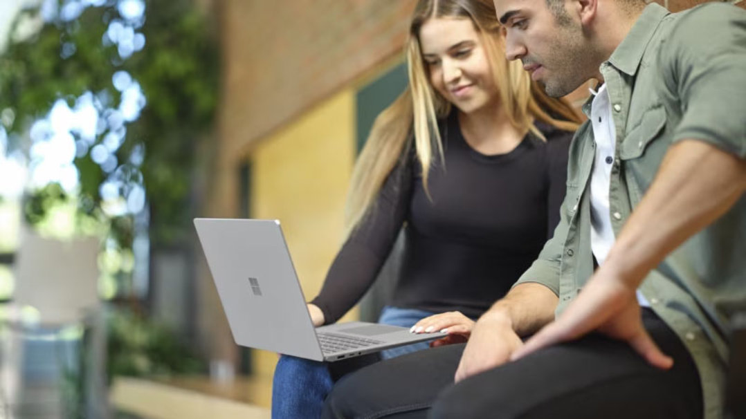 Una donna seduta accanto a un uomo guarda il suo laptop Surface