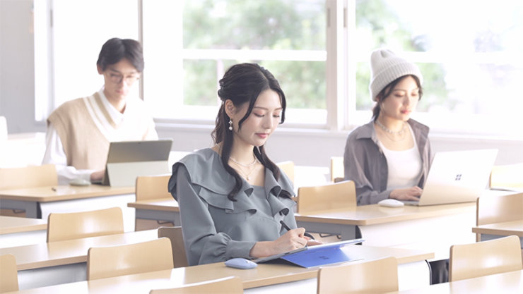 講義室でノート PC で勉強する 3 人の学生