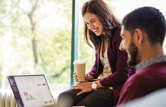 A person holding a cup of coffee and a person looking at a computer