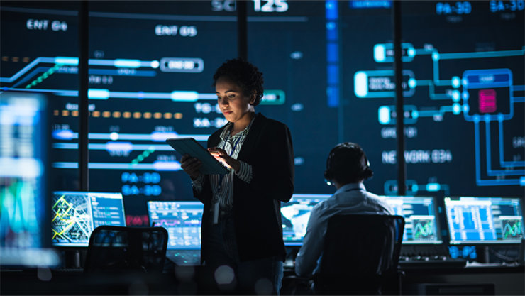 woman looking at a tablet in a control room.]