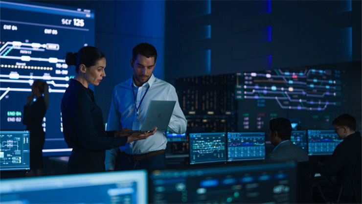 Male and female coworkers looking at laptop in mission control room