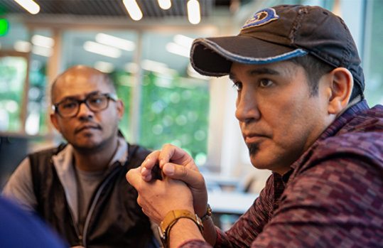 Two men listening to someone speaking in a meeting who isn’t pictured