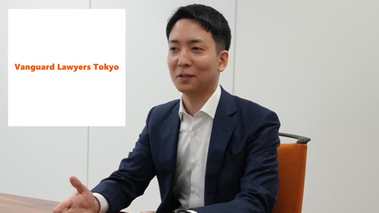 ダークスーツを着た男性が話し、ジェスチャーをしており、左にはオレンジ色の「Vanguard Lawyers Tokyo」のロゴがある。