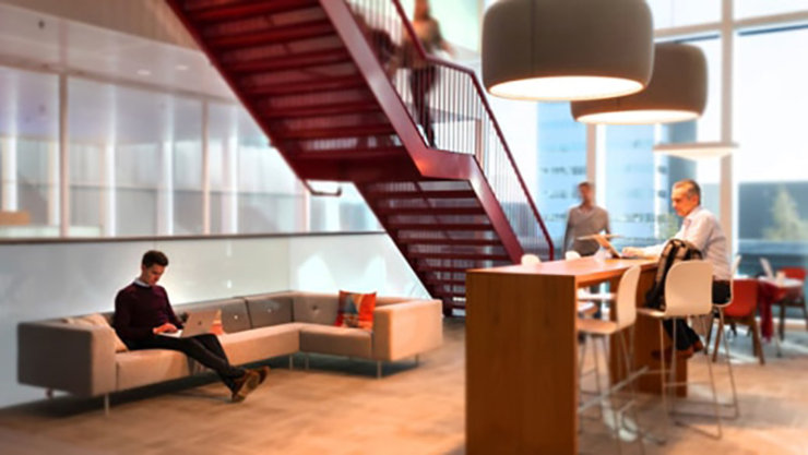Ingang van het Customer Experience Center waar verschillende personen aan het werk zijn op een bank en aan een bartafel Er is tevens een rode trap die naar de eerste verdieping leidt.