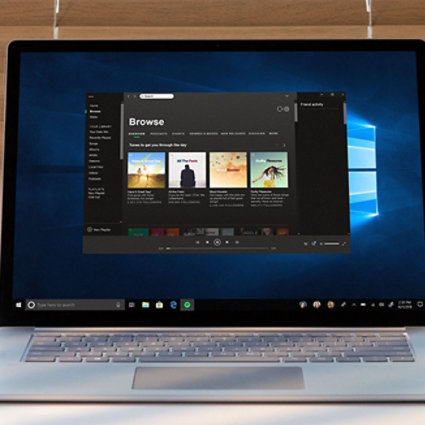 机の上のシルバーのノートパソコンで、音楽ストリーミングサービスが開いています。