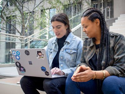 Two people sitting on steps outdoors and looking at a Surface laptop together