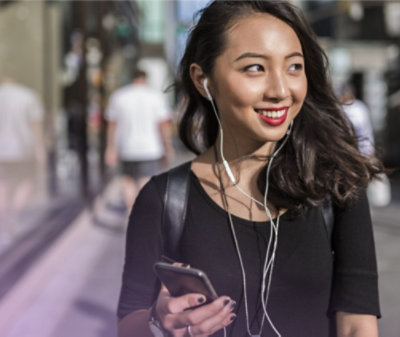 インイヤー ヘッドフォンを装着し、携帯電話を手に笑顔で通りを歩いている人 