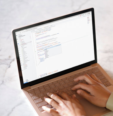 Hands typing on a laptop displaying lines of code