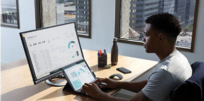 A person typing on a Surface device connected to a desktop monitor at their desk