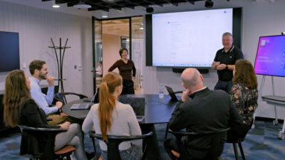 A man standing at a podium, in the background multiple pictures are displayed on the screen.