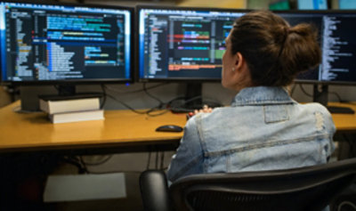A person sitting at a desk looking at three monitors displaying information.