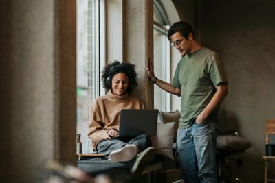 Two people with one person working on a computer with headphones on