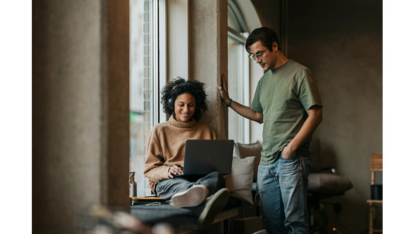 Two people with one person working on a computer with headphones on