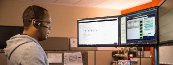 ヘッドセットを装着してデスクで複数の画面を使って作業している人